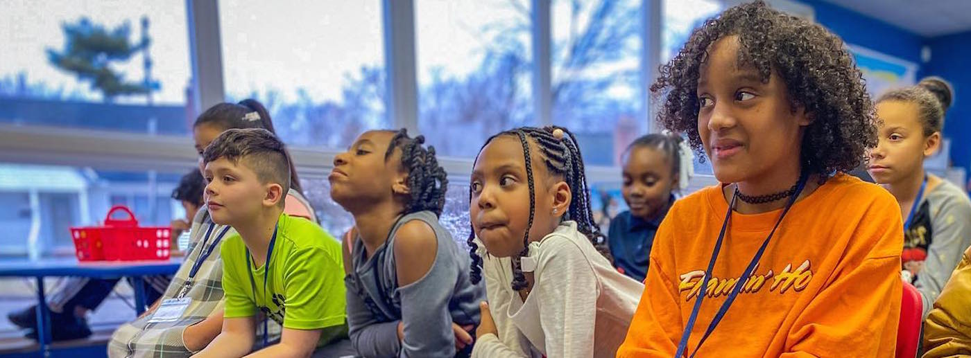 Several young students sit in a row, looking forward.