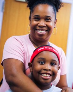 An adult stands with her hands on a young student's shoulders as they smile at the camera.