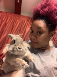 A person holds a fluffy, tan rabbit while both look at the camera.