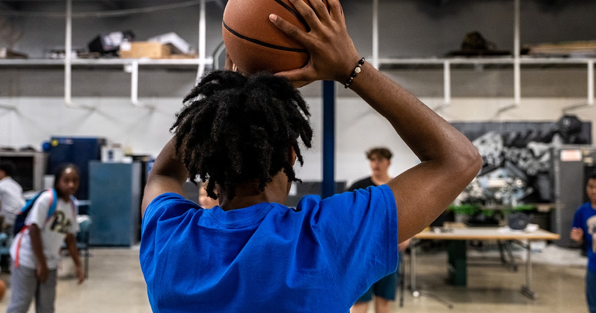 A student holds a basketball above their head.